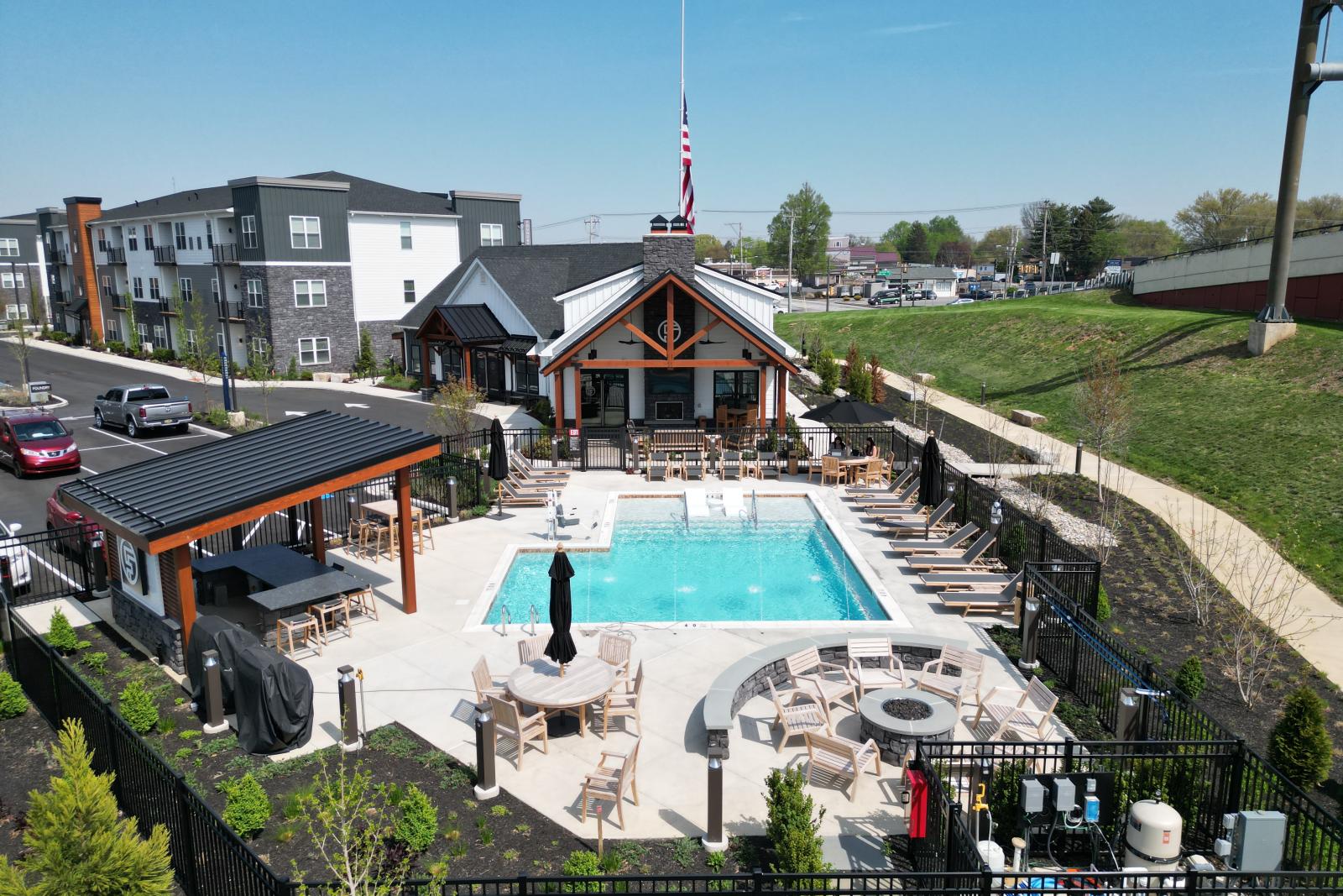 Aerial view of The Foundry’s outdoor amenities, showcasing the resort-style swimming pool, shaded lounge areas, fire pit, and clubhouse surrounded by modern apartment buildings.