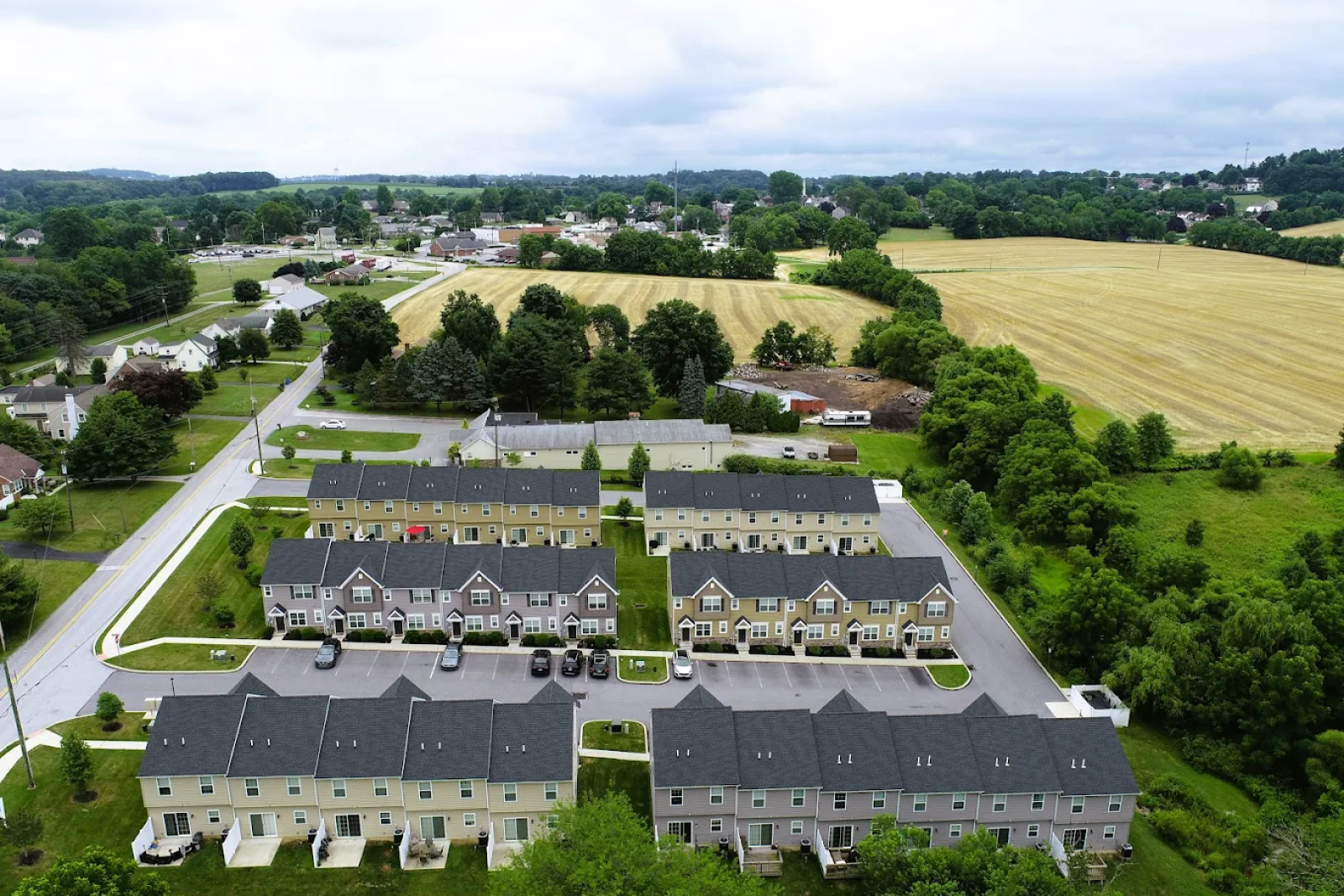 Aerial view of Hunters Pointe townhome apartments in a peaceful rural setting in Pennsylvania, featuring multiple rows of charming two-story residences with green space, parking, and surrounding farmland and trees.